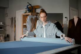  fashion designer or seamstress unrolling a bolt of blue fabric on a cutting table.