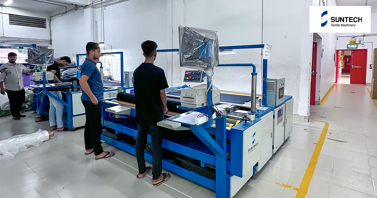 Textile workers operate a fabric relaxing machine in a factory setting.